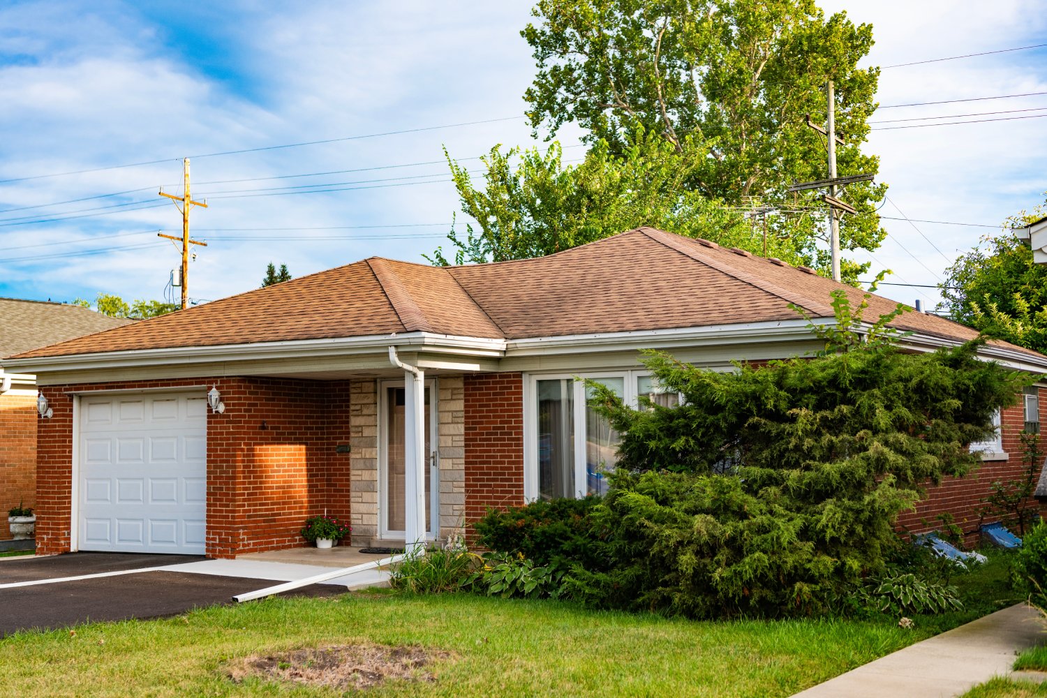 Exterior view of a single-story brick house with a garage, front yard, and mature landscaping – JP Buys SD