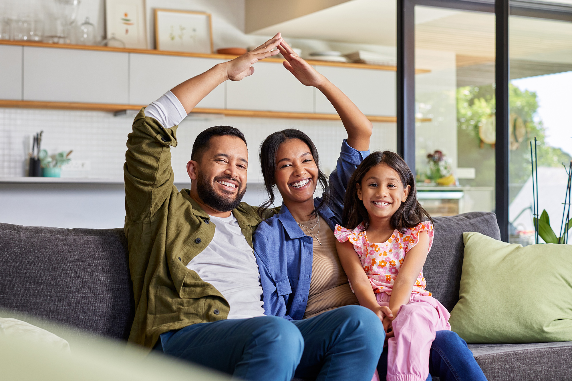 Smiling family sitting together on the couch forming a roof shape with their hands, celebrating a fast and successful home sale in Vista – We Buy Houses Vista
