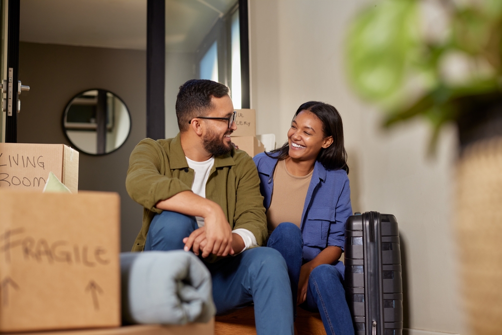 Smiling couple sitting among moving boxes and luggage after selling their house fast in Vista, California – We Buy Houses Vista